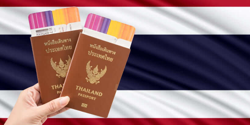 A hand holds two Thai passports against the backdrop of the Thai national flag, colorful boarding passes peeking out. Whether acquiring a Thailand visa from Dubai or elsewhere, adventure awaits with these essential travel documents.